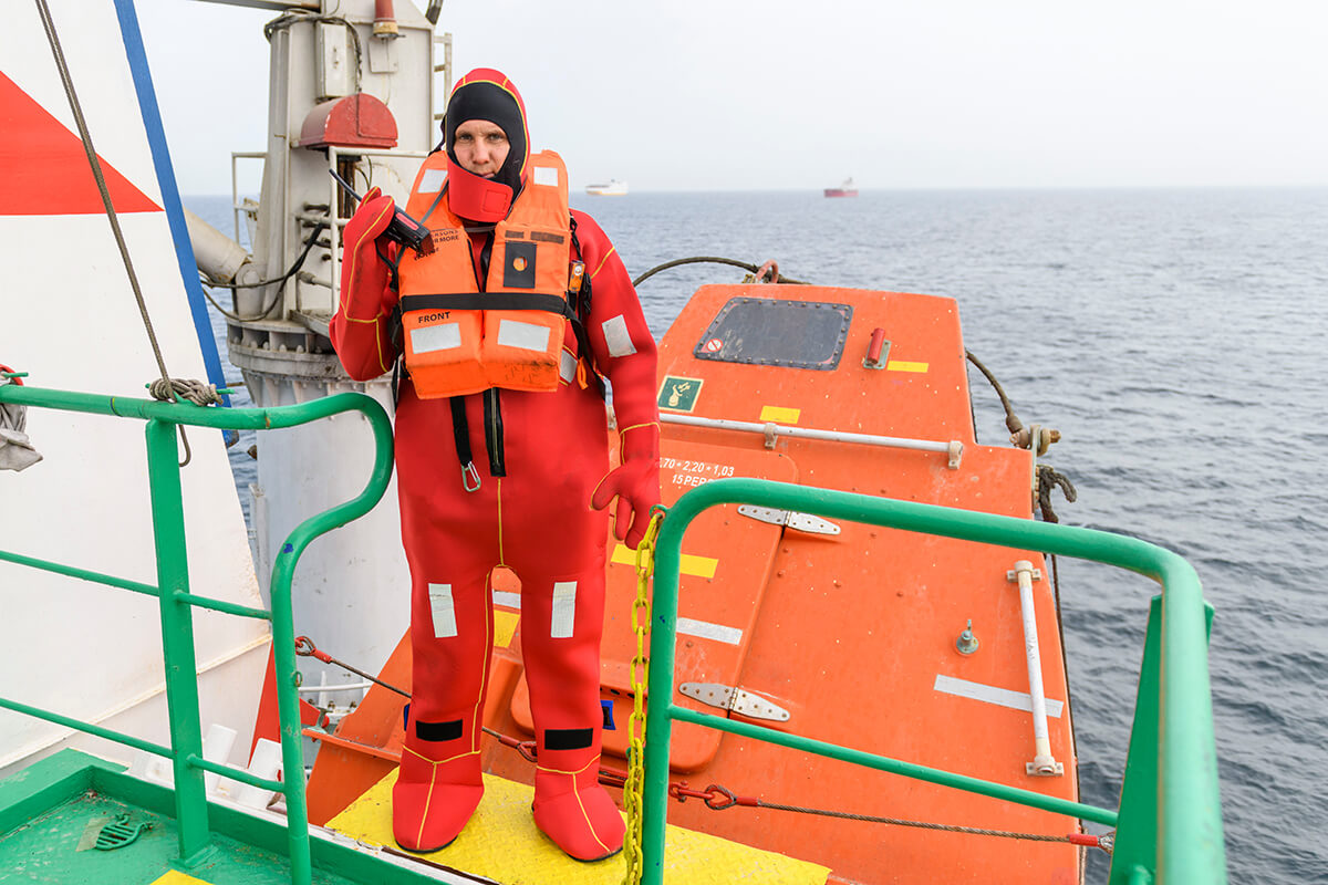 Seaman wearing Immersion Suit on Muster station. Abandon ship drill. Free fall boat. Cargo vessel.